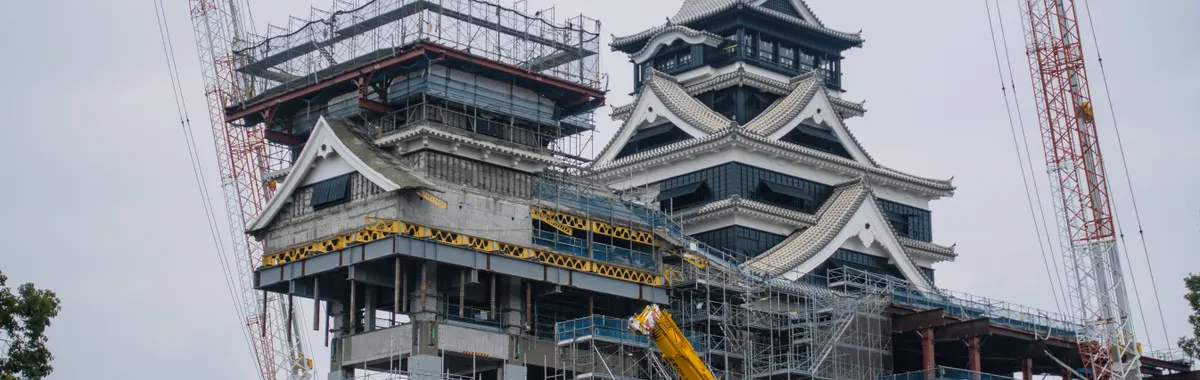 Kumamoto Castle undergoing restoration with cranes and scaffolding visible against the skyline.