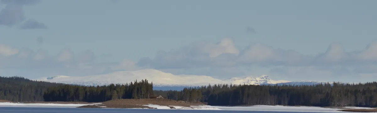 שוודיה: Serene winter landscape with snowy mountains, frozen lake, and blue sky in Sweden.
