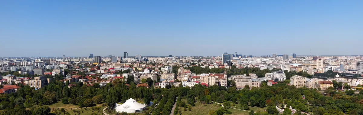 Aerial view of Bucharest cityscape with green parks and skyline under clear blue sky.