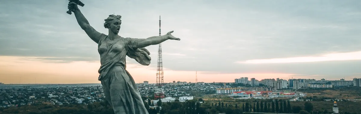 Dramatic aerial view of The Motherland Calls statue in Volgograd at sunrise, overlooking the cityscape.
