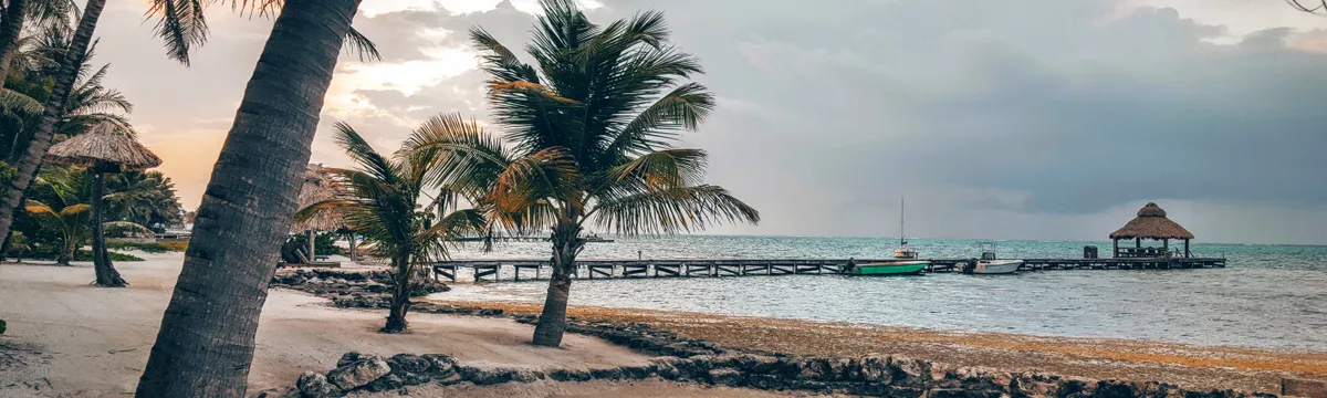 בליז: Scenic tropical beach with palm trees and a wooden pier in San Pedro, Belize at sunset.
