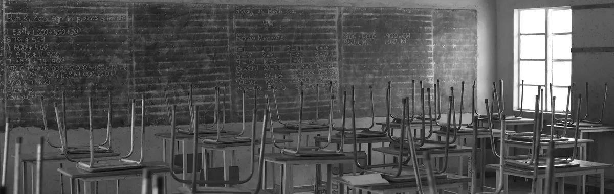 Grayscale image of an empty classroom in Bulawayo, Zimbabwe, with desks and chairs arranged neatly.