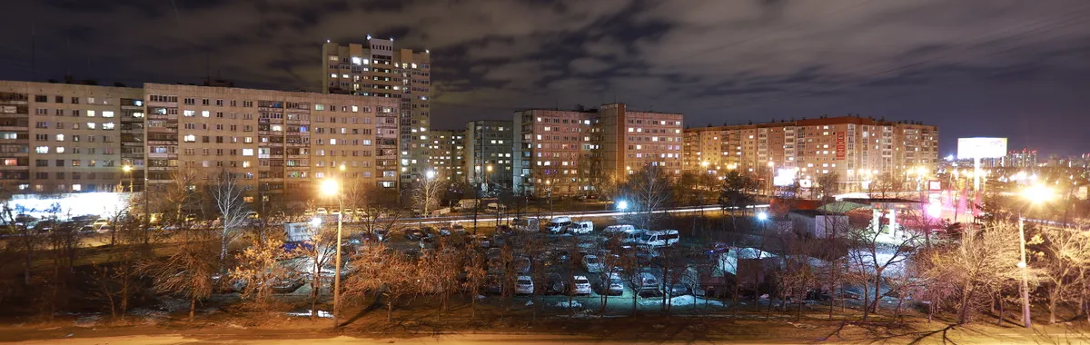 A vibrant cityscape of Chelyabinsk at night showcasing illuminated apartments and streetlights.