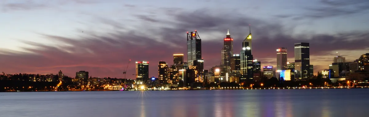 A breathtaking view of Perth's illuminated skyline reflecting on the calm water at dusk.
