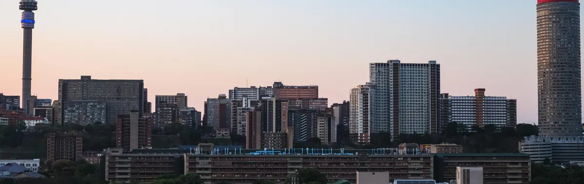 A panoramic view of Johannesburg cityscape during sunset, featuring modern skyscrapers and iconic towers.