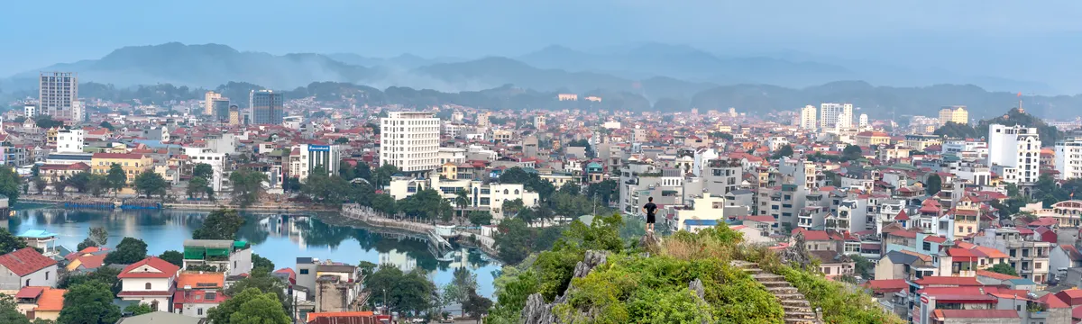 וייטנאם: Aerial view of Lang Son cityscape with lush green hill and distant mountains under a cloudy sky.