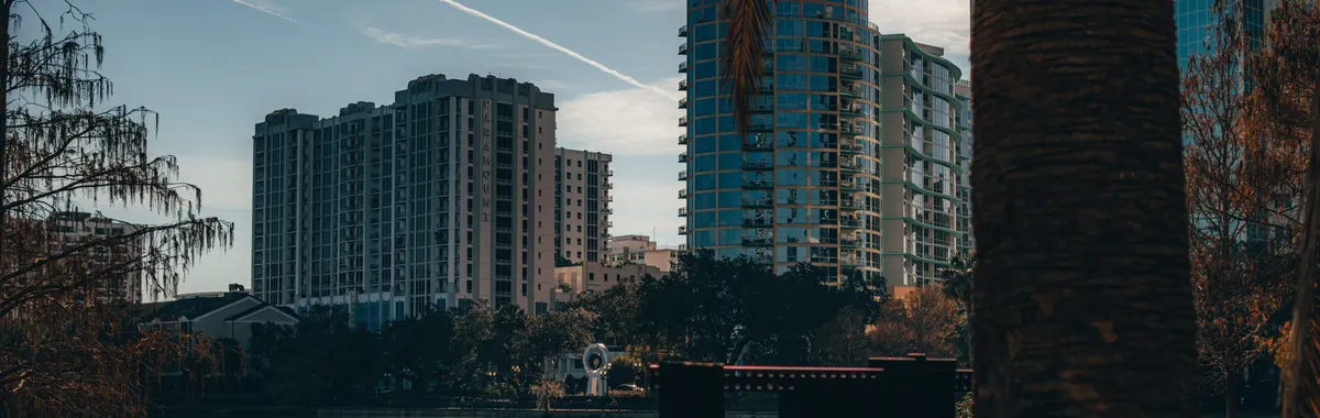 View of Orlando's modern skyline reflecting on a tranquil lake, surrounded by trees.