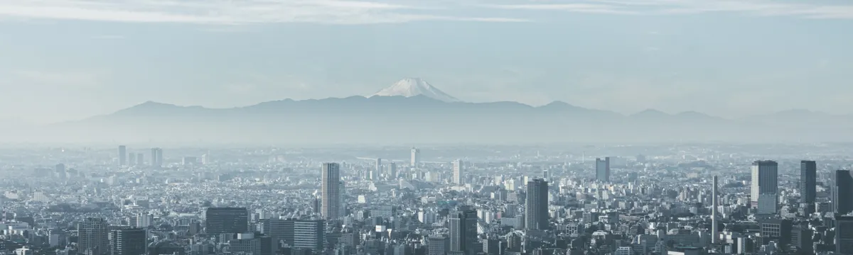 יפן: Panoramic view of Tokyo cityscape with Mount Fuji looming in the background, under cloudy skies.