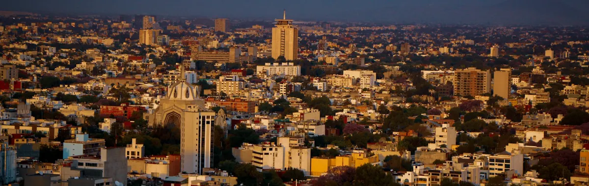 Aerial view of Guadalajara cityscape during sunset, showcasing vibrant buildings and warm colors.