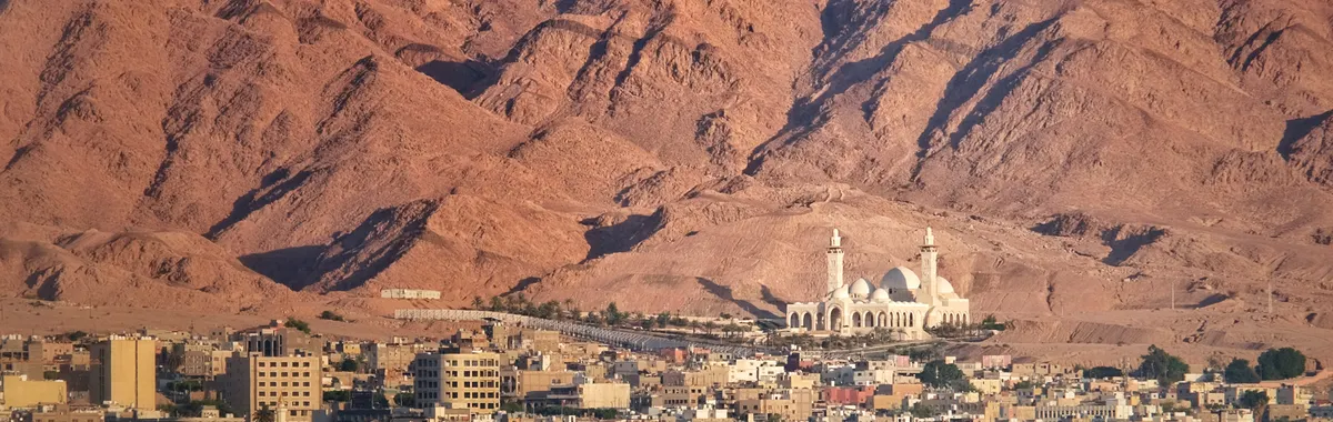 A scenic view of Aqaba city against a dramatic mountain backdrop by the sea.
