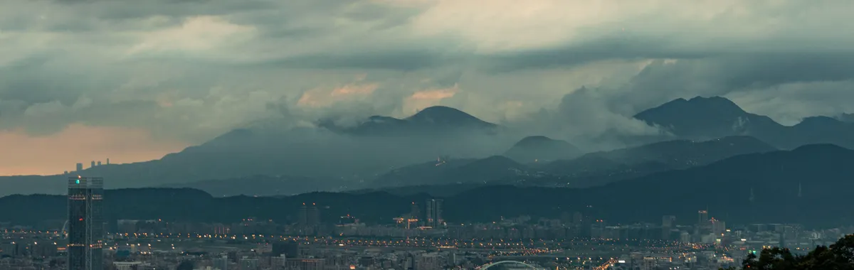 Aerial view of Taipei's skyline featuring skyscrapers and moody clouds over mountains.