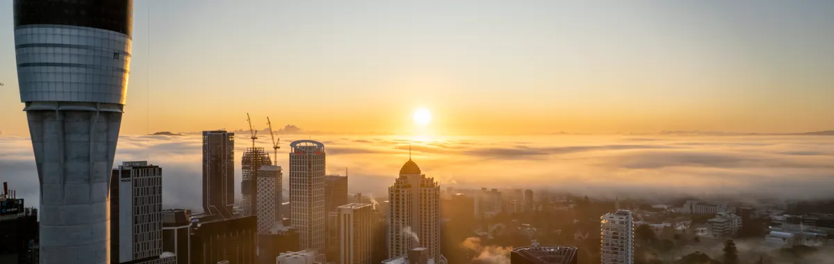 A stunning view of Auckland's skyline with the Sky Tower at sunrise, enveloped in morning fog.
