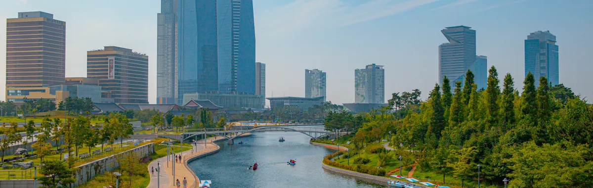 A scenic view of a modern urban skyline with a river flowing through a park in Incheon, South Korea.
