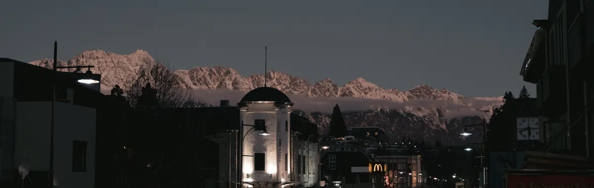 Discover Queenstown's charming streets against a majestic mountain backdrop at dusk.