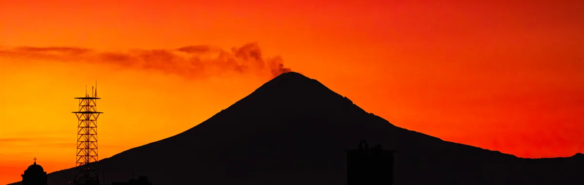 Dramatic silhouette of Popocatépetl volcano with vibrant red and orange sunset sky in Puebla, Mexico.