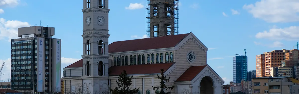 Catholic Cathedral surrounded by modern cityscape in Pristina, an architectural landmark blending past and present.