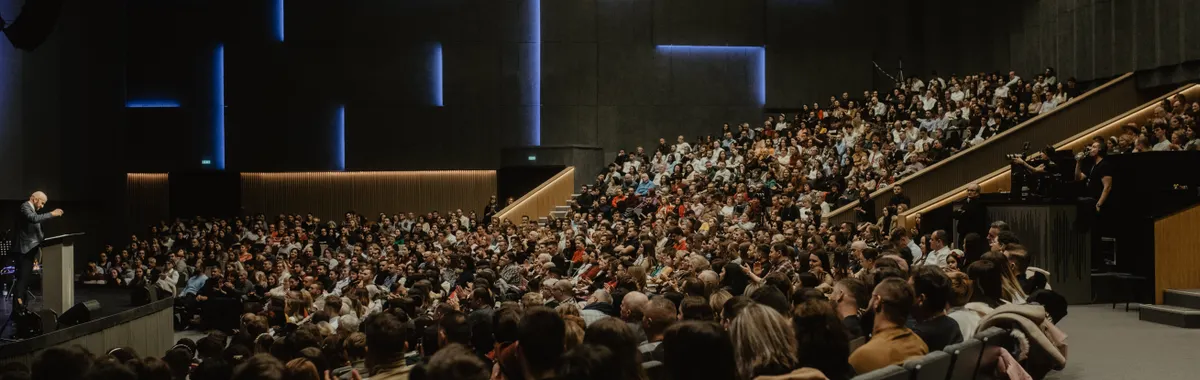 A large audience attentively listens to a speaker at a conference in Oradea, Romania.