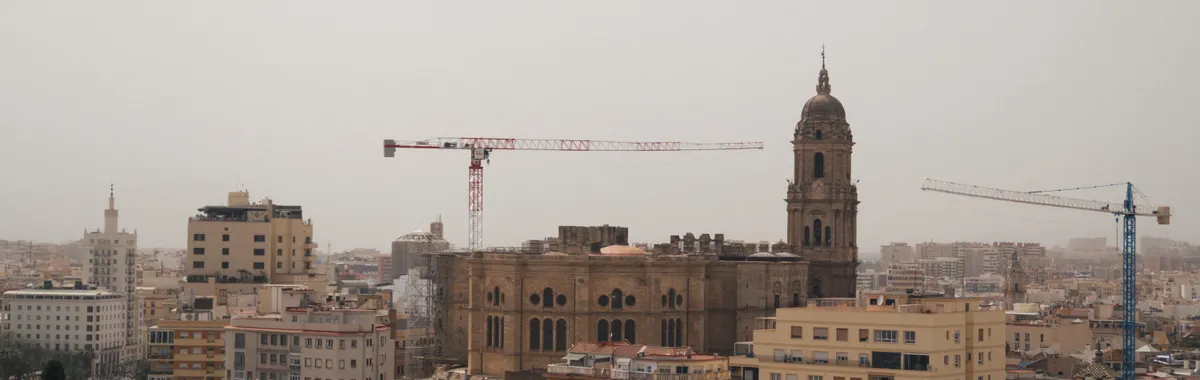 A stunning urban landscape featuring Malaga Cathedral amidst cranes and city buildings.