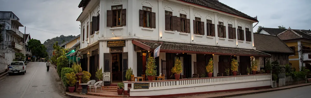 Elegant colonial-style building at a street corner in Luang Prabang, Laos, under cloudy skies.