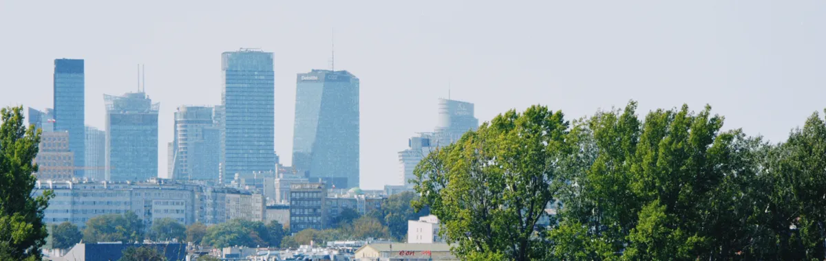 Skyline of Warsaw with modern buildings and a train passing amidst the greenery.