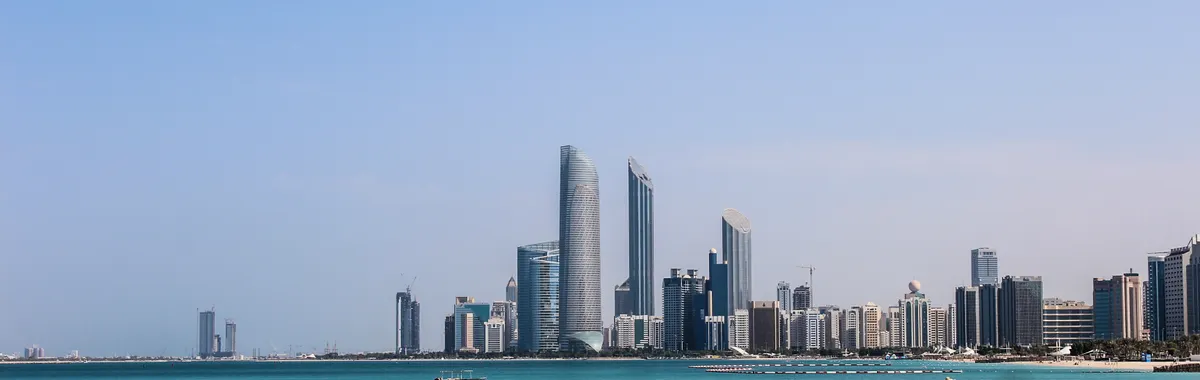 Stunning view of the Abu Dhabi skyline reflecting in the calm Gulf waters on a sunny day.