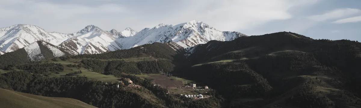 קירגיזסטן: Explore the serene landscape of snow-capped mountains and yurts in Kyrgyzstan's expansive countryside.