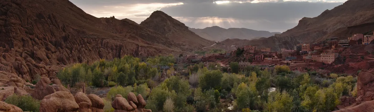 מרוקו: Beautiful valley in Morocco with lush greenery and rocky mountains under a twilight sky.