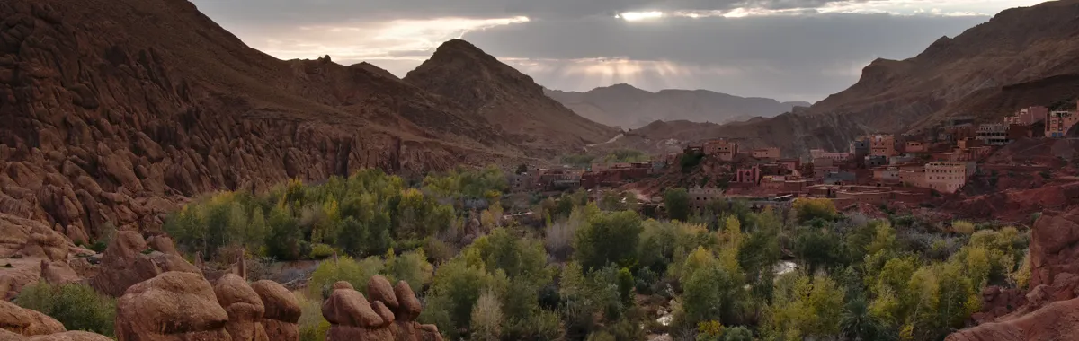 מרוקו: Beautiful valley in Morocco with lush greenery and rocky mountains under a twilight sky.