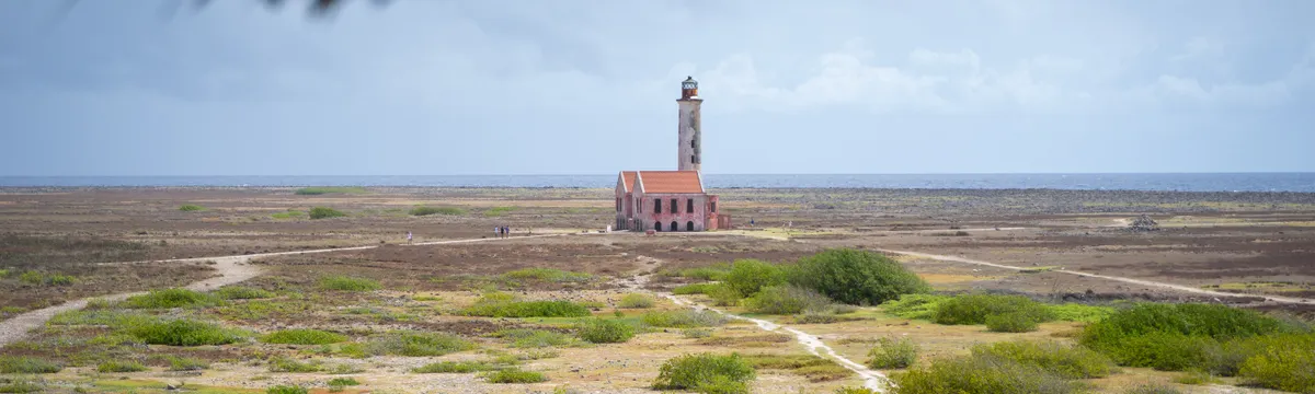 קוראסאו: A distant view of the historic lighthouse on Klein Curaçao with a rugged landscape and sky backdrop.