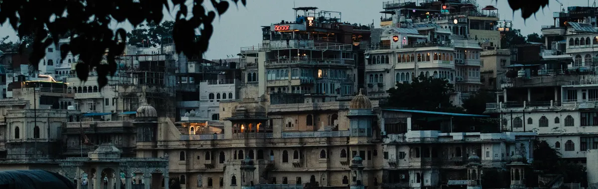Scenic view of Udaipur's City Palace and surrounding architecture seen from Lake Pichola at dusk.