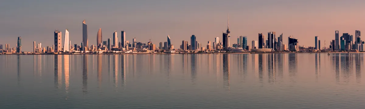 כווית: Beautiful Kuwait City skyline reflected on calm water at sunset, showcasing modern architecture.