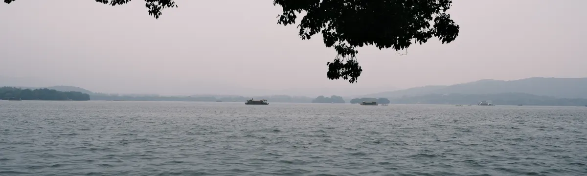 סין: Tranquil scene of West Lake with peaceful waters and distant hills in Hangzhou, China.