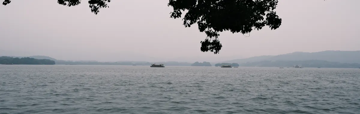 סין: Tranquil scene of West Lake with peaceful waters and distant hills in Hangzhou, China.