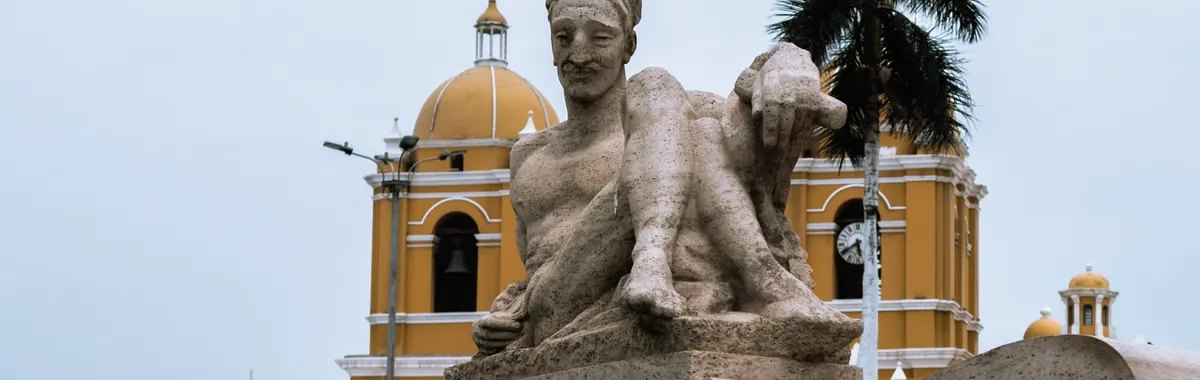 The Plaza de Armas in Trujillo, Peru, featuring a prominent sculpture and colonial architecture under a cloudy sky.