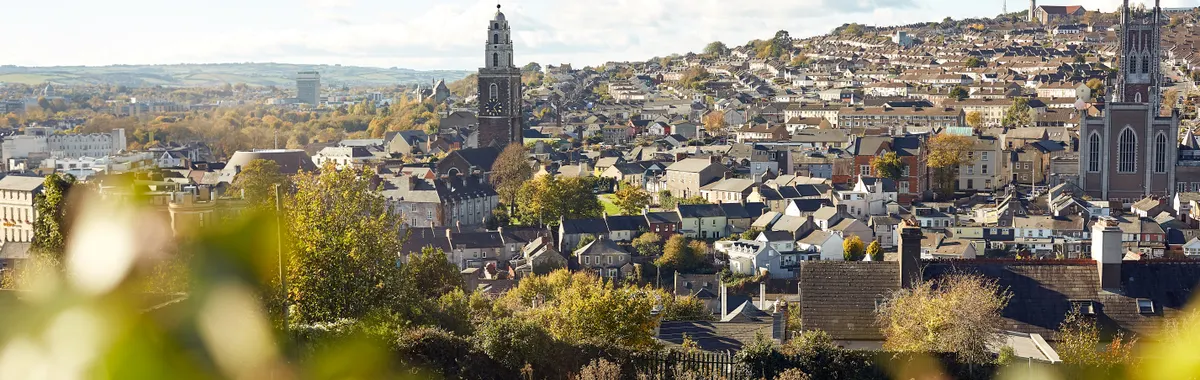 Beautiful view of Cork city with iconic churches and lush greenery, under a bright blue sky.