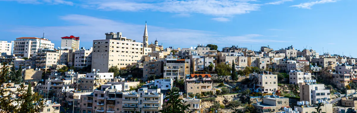 Explore the cityscape of Bethlehem with its distinctive architecture under a bright blue sky, showcasing traditional Middle Eastern urban life.