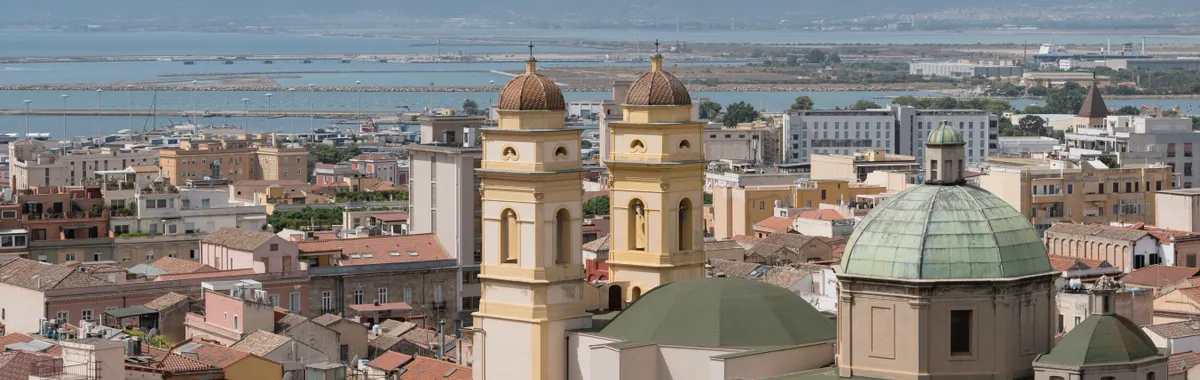 A panoramic view of Cagliari, Italy, featuring historical architecture and the Mediterranean Sea.