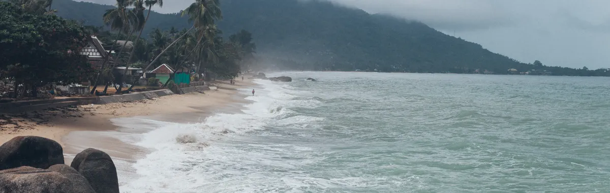 Serene view of a tropical beach in Koh Samui, Thailand, with crashing waves and lush greenery.