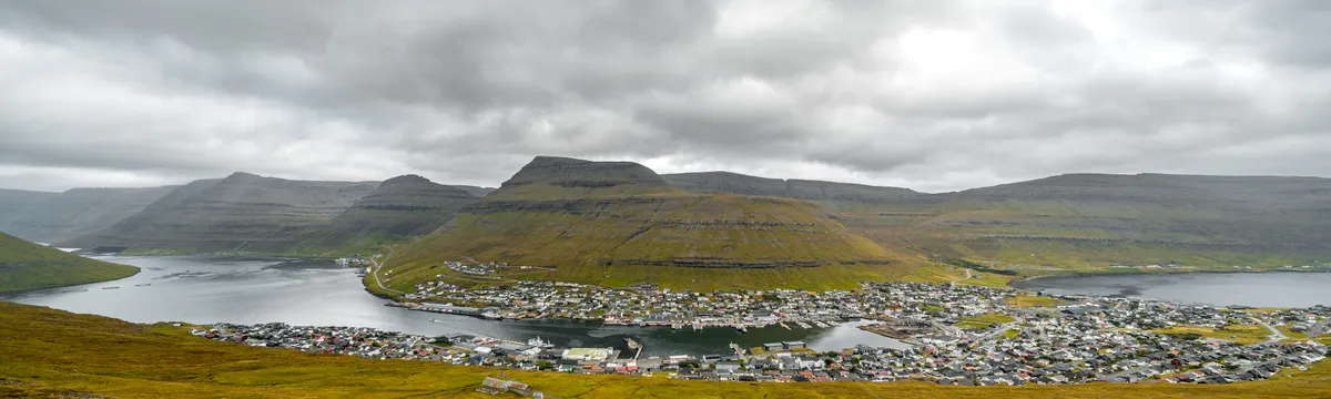 איי פארו: Aerial view of Sandoy Island in the Faroe Islands featuring a serene village landscape and coastal mountains.