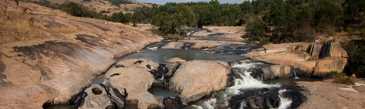 אסוואטיני: Stunning view of rocky cascades and trees along a river in Eswatini, showcasing natural beauty and tranquility.