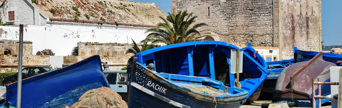 Colorful fishing boats and nets by the historic fort in Essaouira, Morocco, under a clear blue sky.