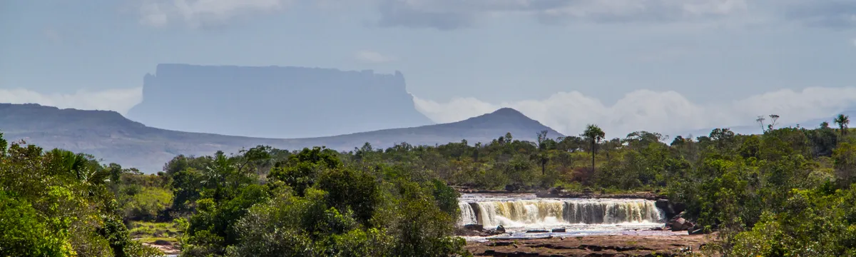 ונצואלה: Breathtaking view of a waterfall with lush greenery and a distant Tepui in Canaima National Park, Venezuela.