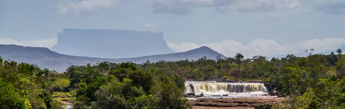 ונצואלה: Breathtaking view of a waterfall with lush greenery and a distant Tepui in Canaima National Park, Venezuela.