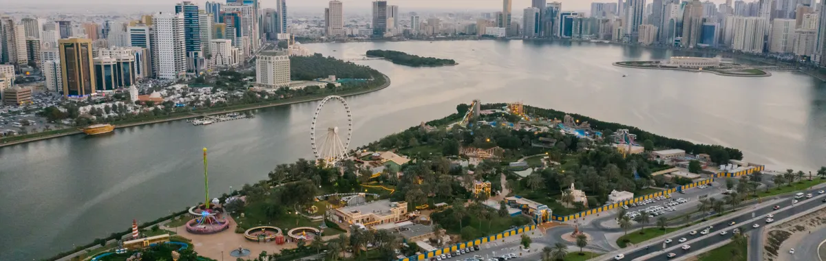 A stunning aerial shot of Sharjah cityscape featuring parks, landmarks, and coastline at sunset.