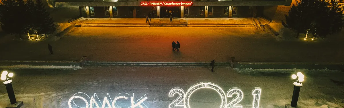Aerial shot of illuminated Omsk theater during winter night with snow and festive lights.