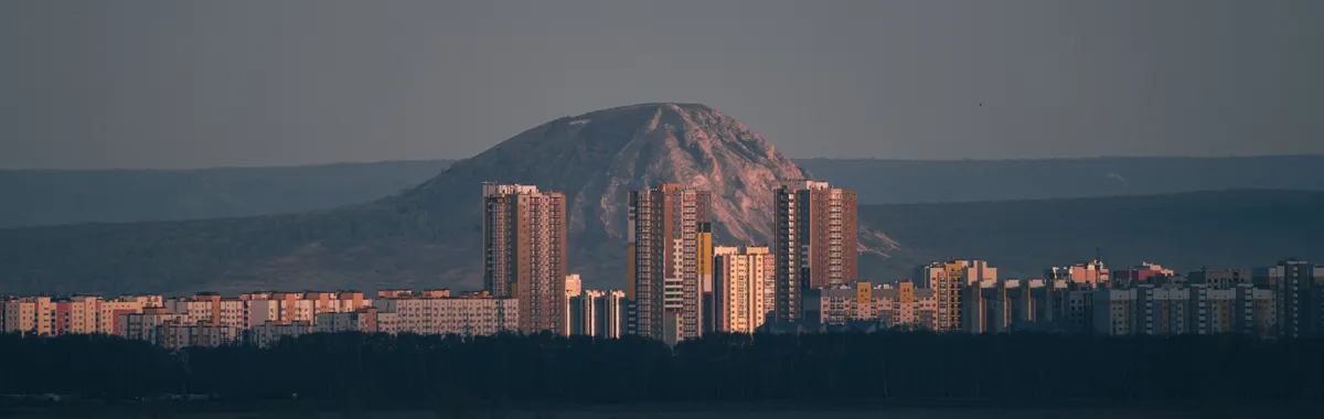 A stunning cityscape of Ufa at dusk showcasing high-rise buildings and a mountain backdrop.