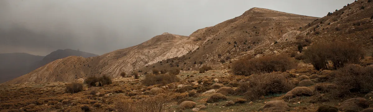 איראן: A rugged mountainous landscape under a cloudy sky in Tehran, offering a dramatic and earthy scene.