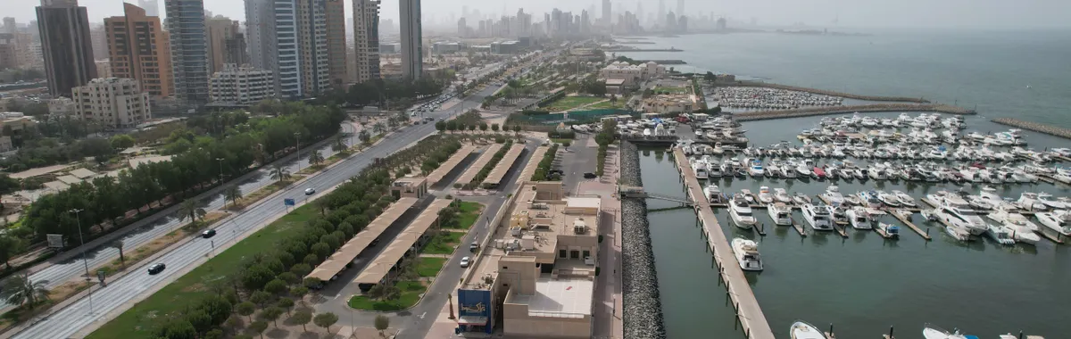 Aerial view of Kuwait City's modern skyline and bustling harbor with yachts.